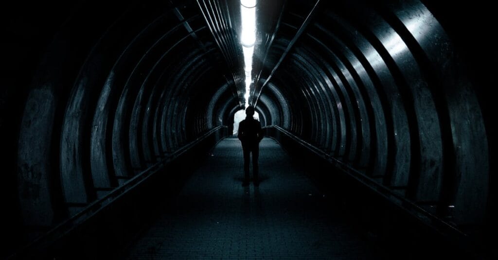 A lone figure stands in a dimly lit tunnel, creating an air of mystery.