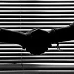 Silhouette of two people shaking hands symbolizing partnership and trust.
