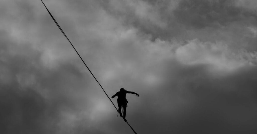 A silhouette of a person balancing on a tightrope against a dramatic, cloudy sky.