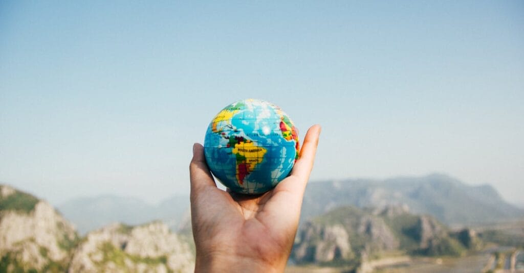 Hand holding a globe against a mountain background symbolizing travel and exploration.