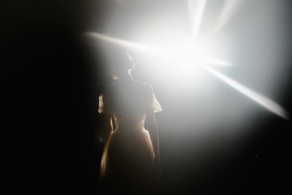 A graceful ballerina stands in silhouette under a dramatic, bright spotlight.