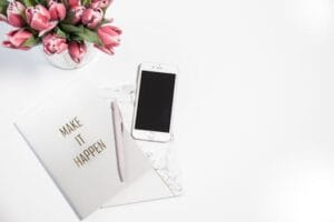 A minimalist desk setup featuring a smartphone, pink tulips, and a motivational notepad.